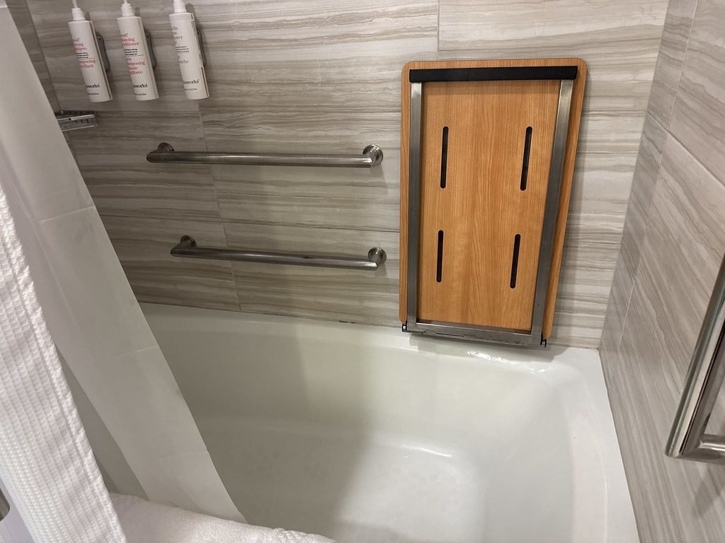Bathroom with grab bars and a fold-down wooden shower seat for safe everyday use