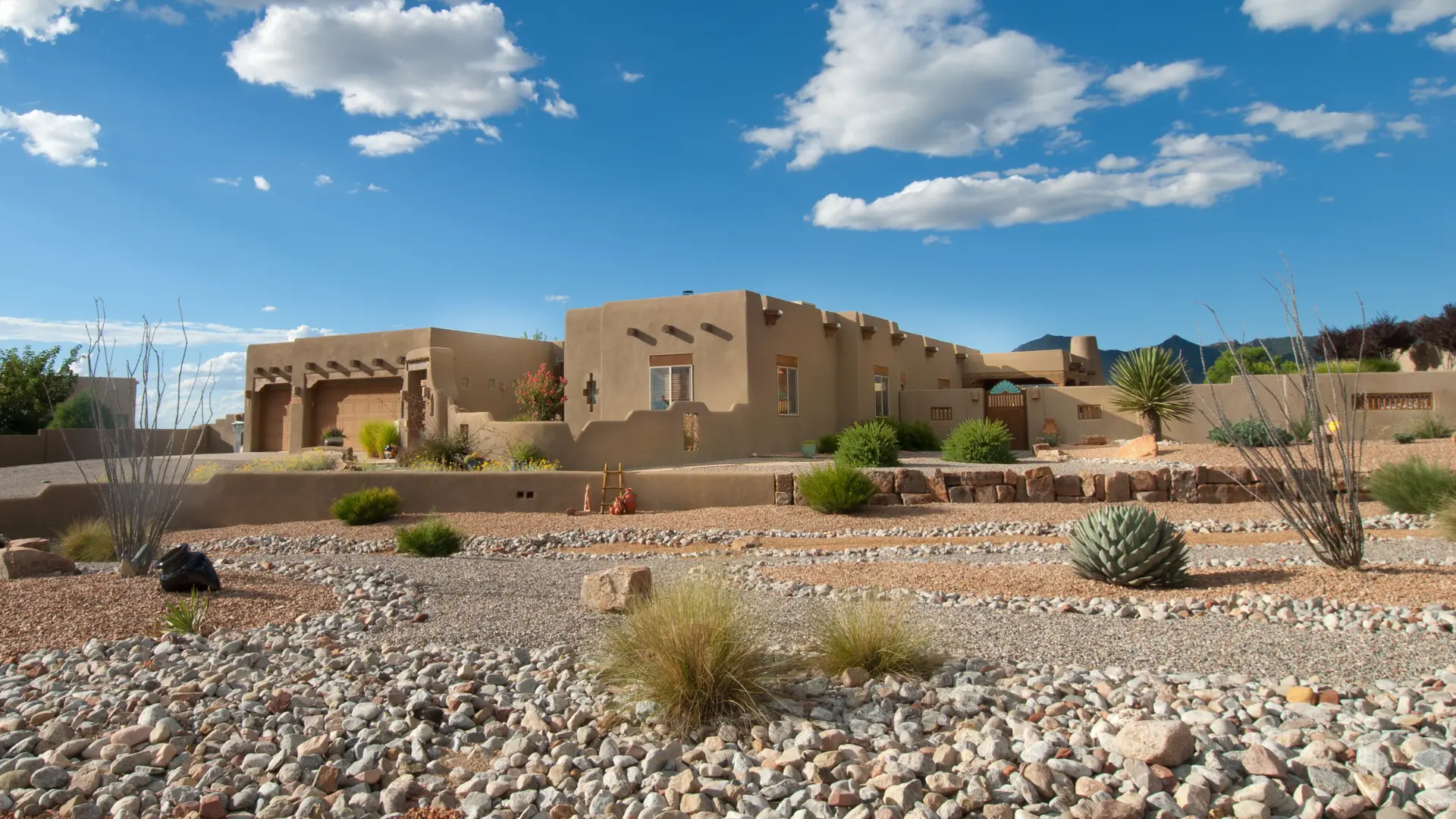 An earth-toned house with a rocky front garden, sparse grasses and desert plants.