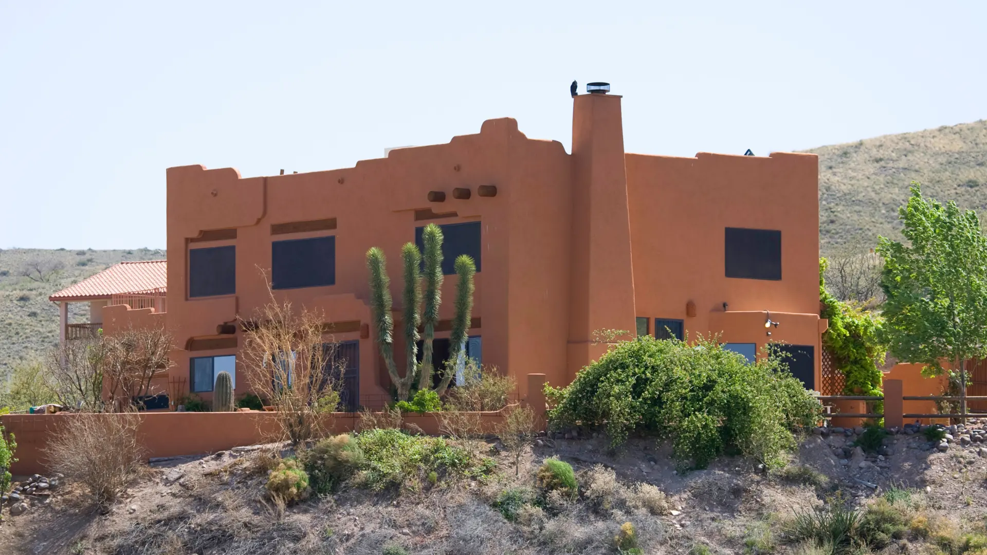 An earth-toned house with flat roofs, cacti and a rocky desert landscape, illustrating Mexican house styles.