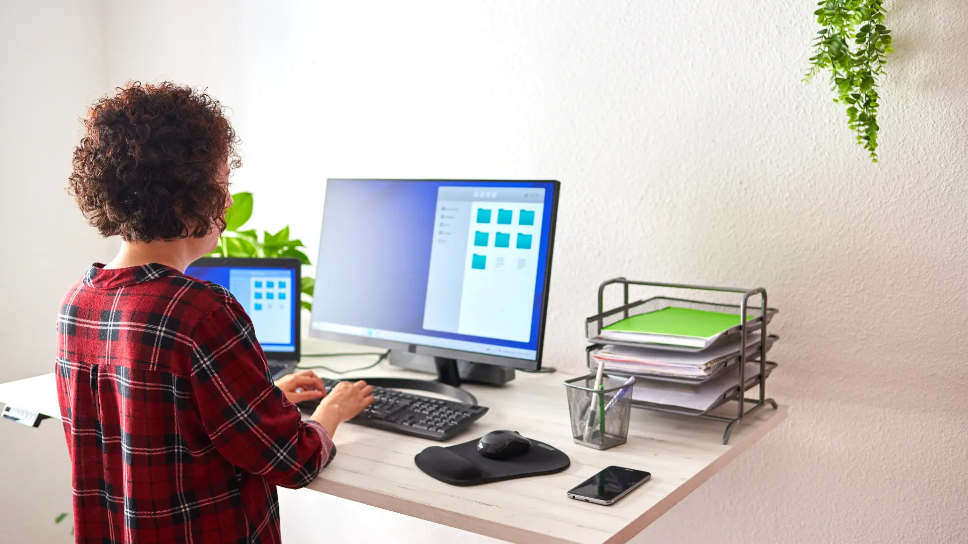 A person seated at a white home-office desk with a monitor, keyboard and document trays.