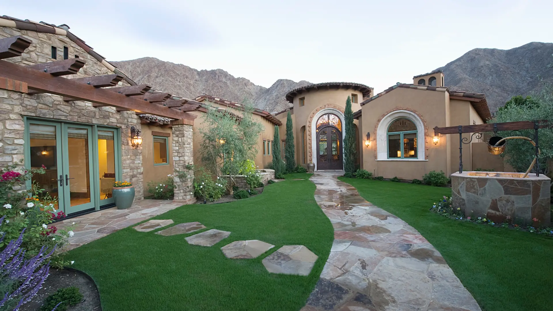 A house courtyard with a curved stone path, garden lawn and arched entrance, illustrating a guide to Mexican house styles.