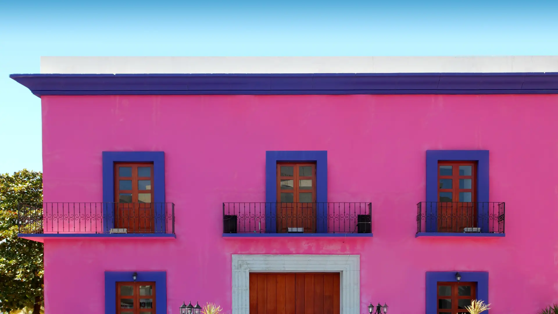 A bright pink house facade with small metal balconies and timber-framed windows, illustrating Mexican house styles.