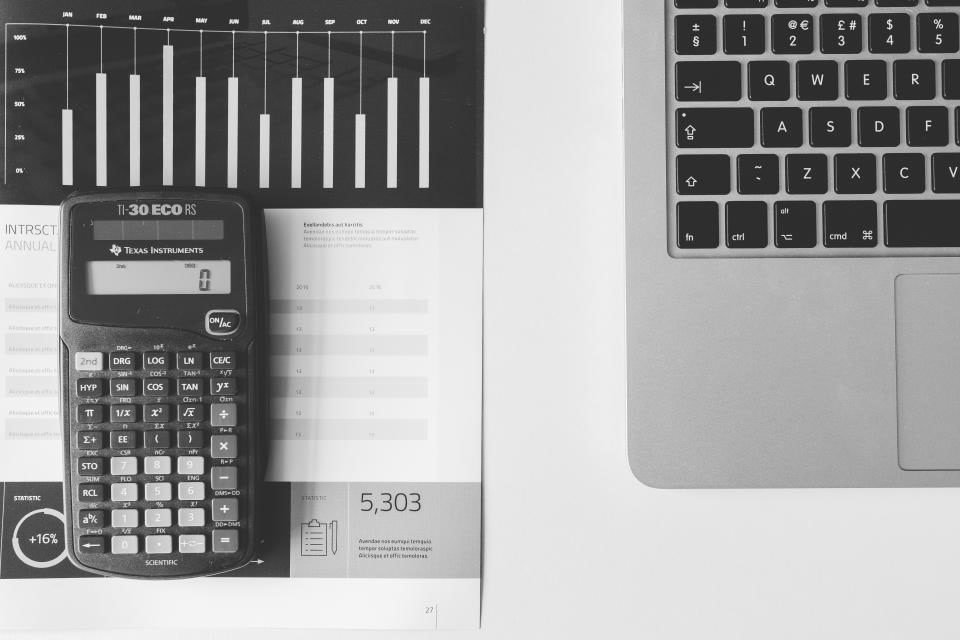 Calculator, printed bar chart and laptop on a white desk
