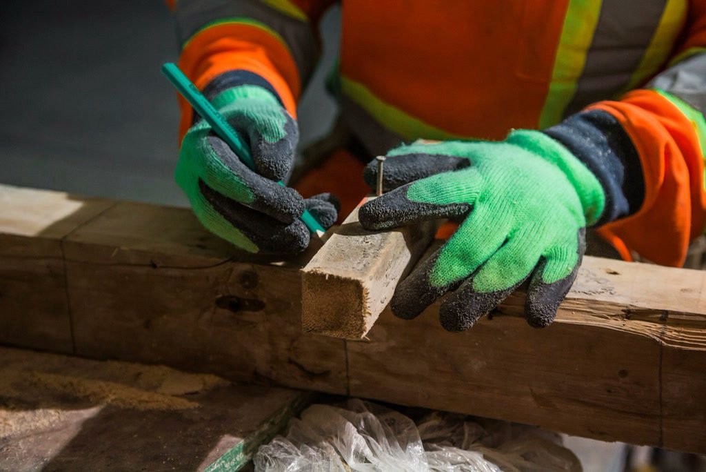 Construction worker in safety gloves marking a timber beam with a pencil