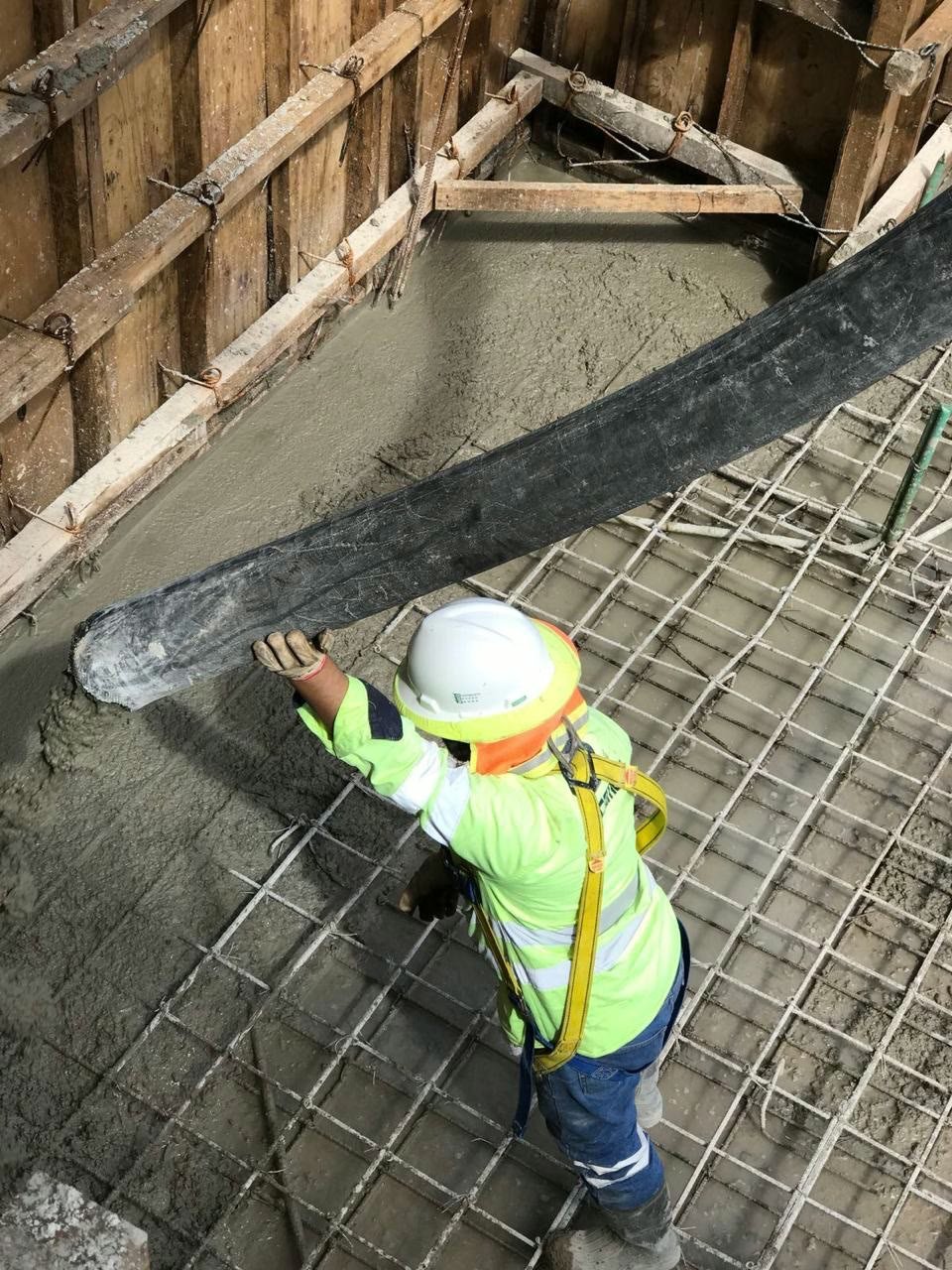 Worker in high-visibility gear placing concrete from a pump hose around the steel reinforcement of a basement foundation.