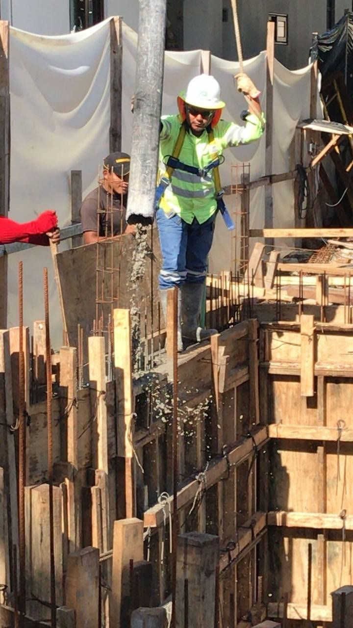 Worker in a hard hat and safety harness guiding a concrete pump hose into the timber formwork and reinforcing steel of a basement wall in Playa del Carmen.