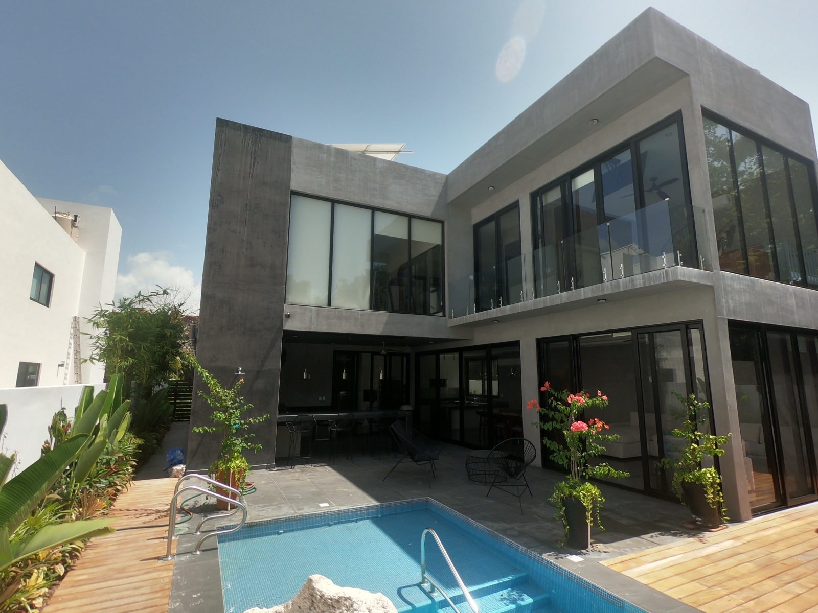 Pool and timber deck beside the concrete facade and upper balcony of Casa Brisas in Playacar.