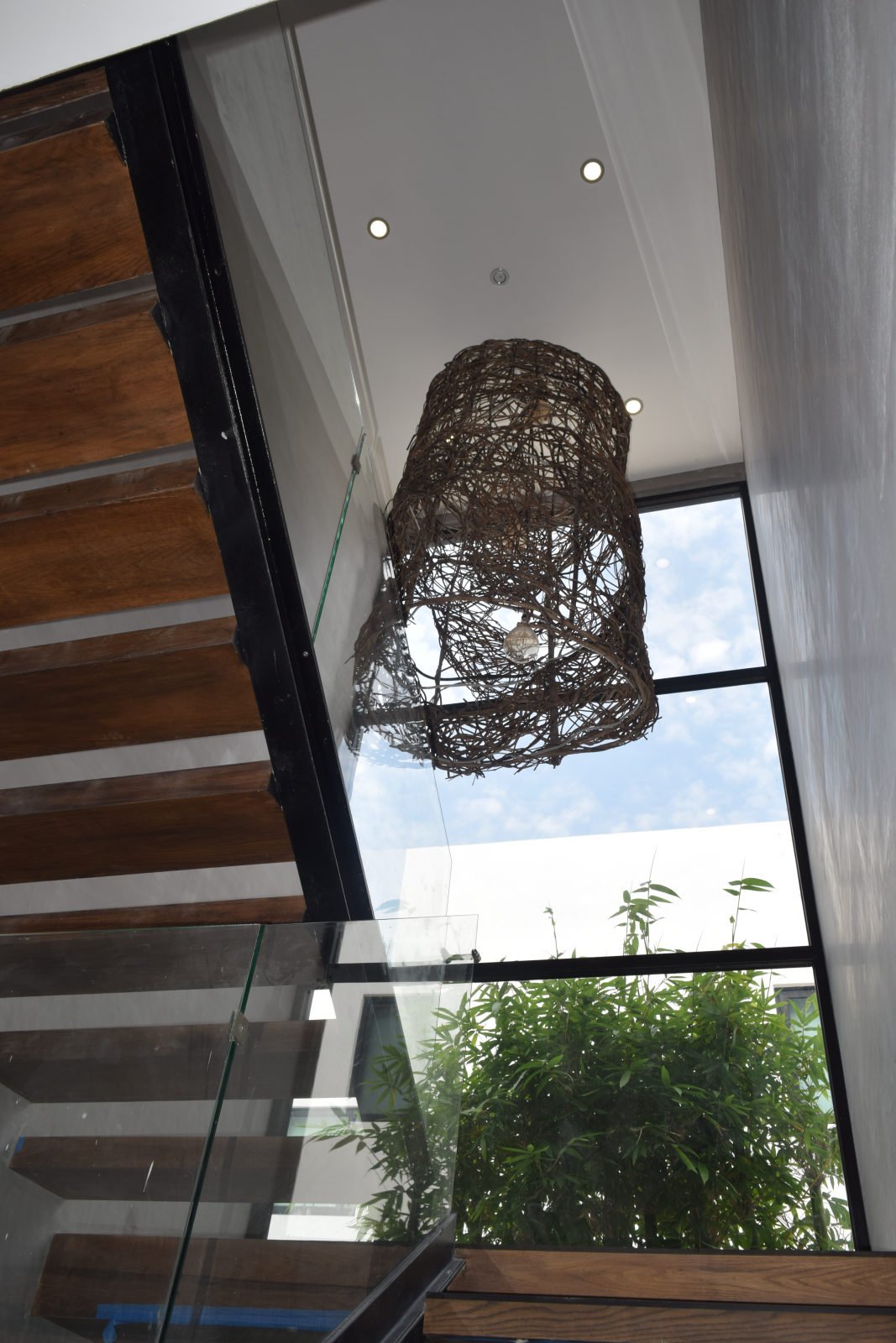Double-height staircase at Casa Brisas in Playacar with a woven pendant light, timber treads and large windows.