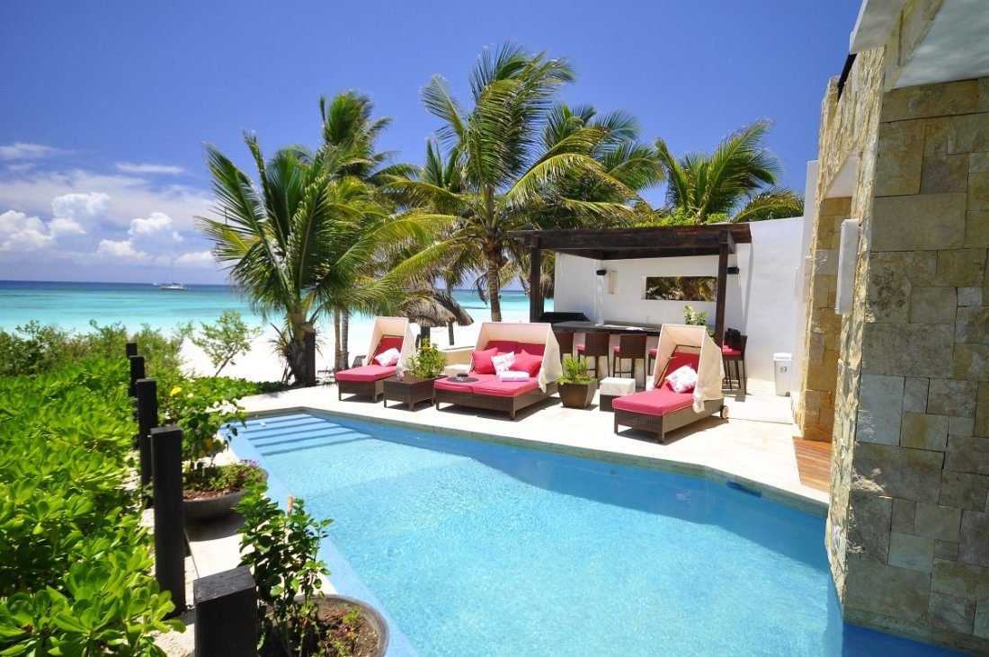 Sereno beachfront pool with red lounge beds, a stone-clad wall, palm trees and the Caribbean beyond.