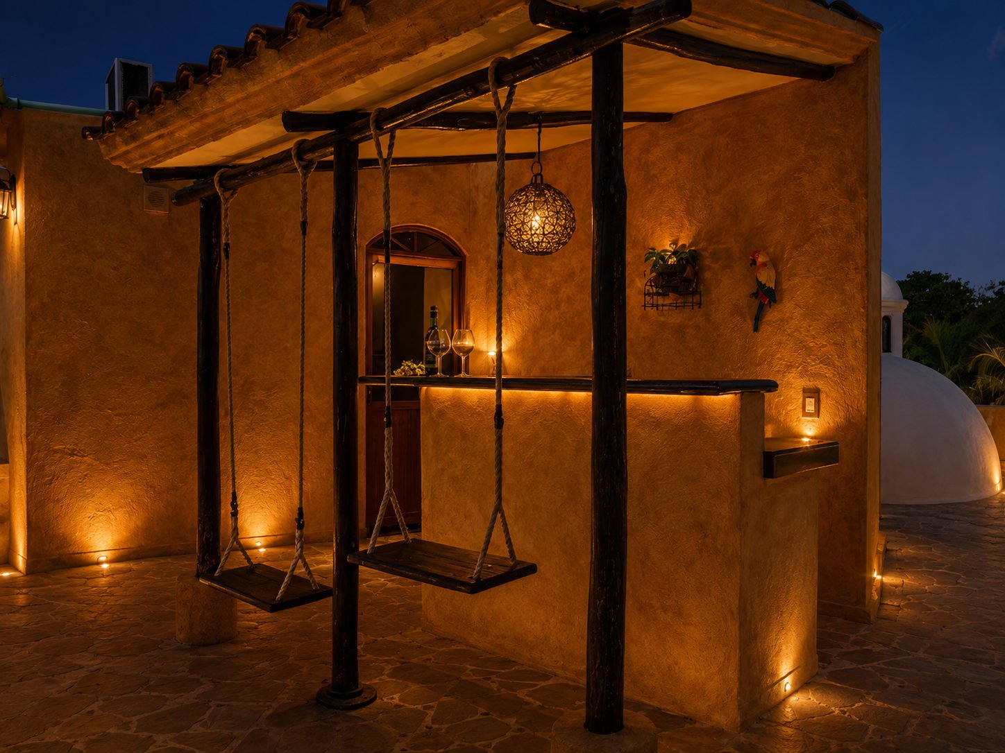 Covered villa patio with a hanging chair, outdoor counter and warm wall lighting.