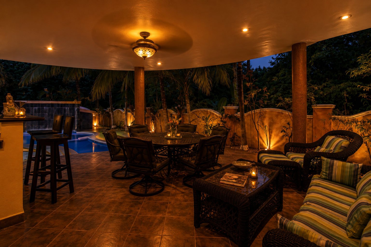 Covered outdoor living area with cushioned seating, dining furniture and a view toward the illuminated pool.