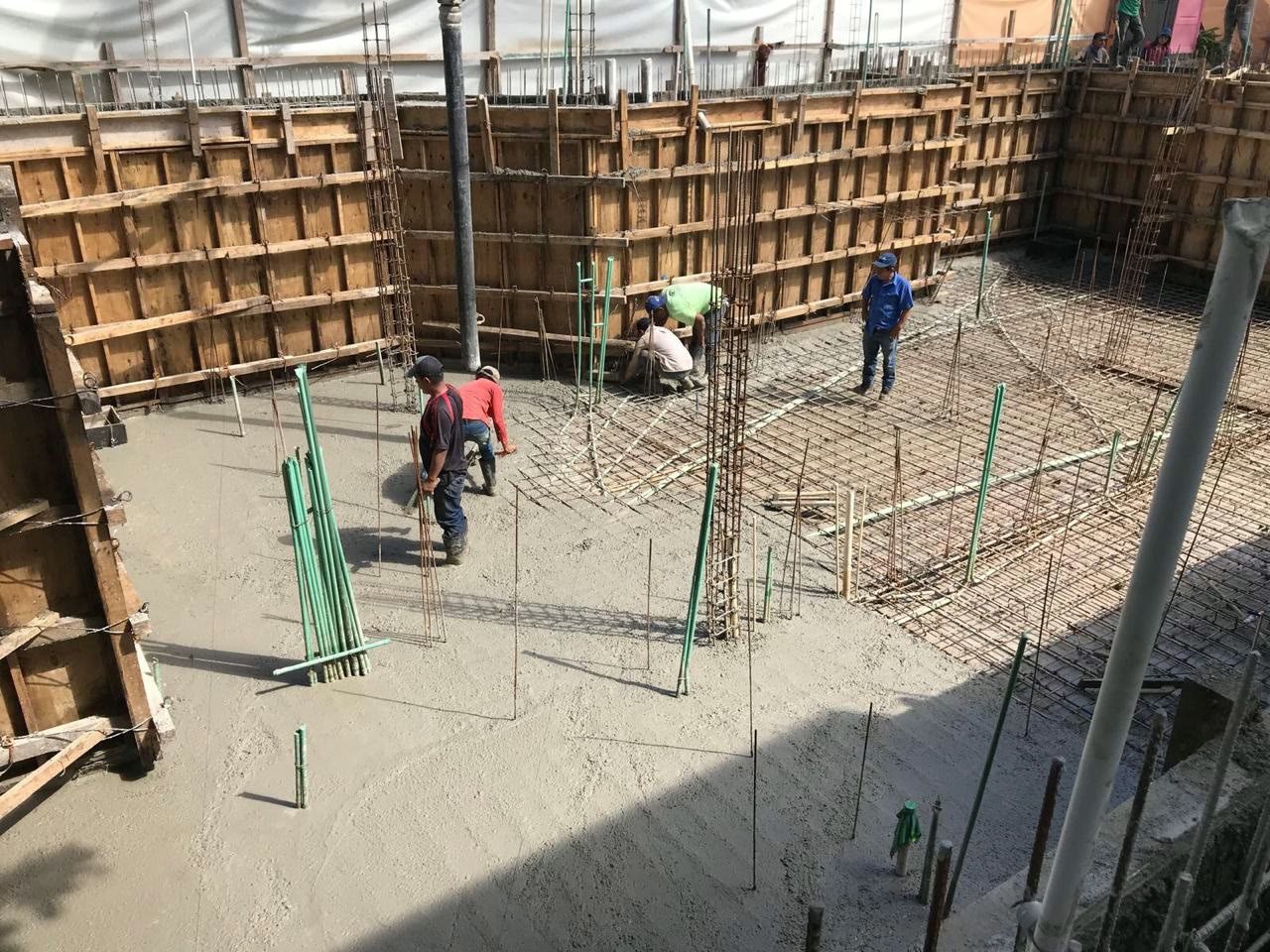 Basement floor slab being poured inside timber wall formwork, with the reinforcing steel grid still exposed across part of the floor, near the beach in Playa del Carmen.